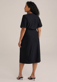 Svart midi-klänning med korta ärmar, texturerad tyg och figurnära midja. Designen har en smidig siluett och en rak nederkant.