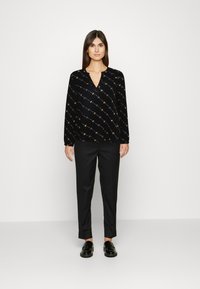 Blusa preta de manga longa com decote em V, featuring um padrão geométrico em várias cores, combinada com calças retas pretas e sapatos confortáveis.