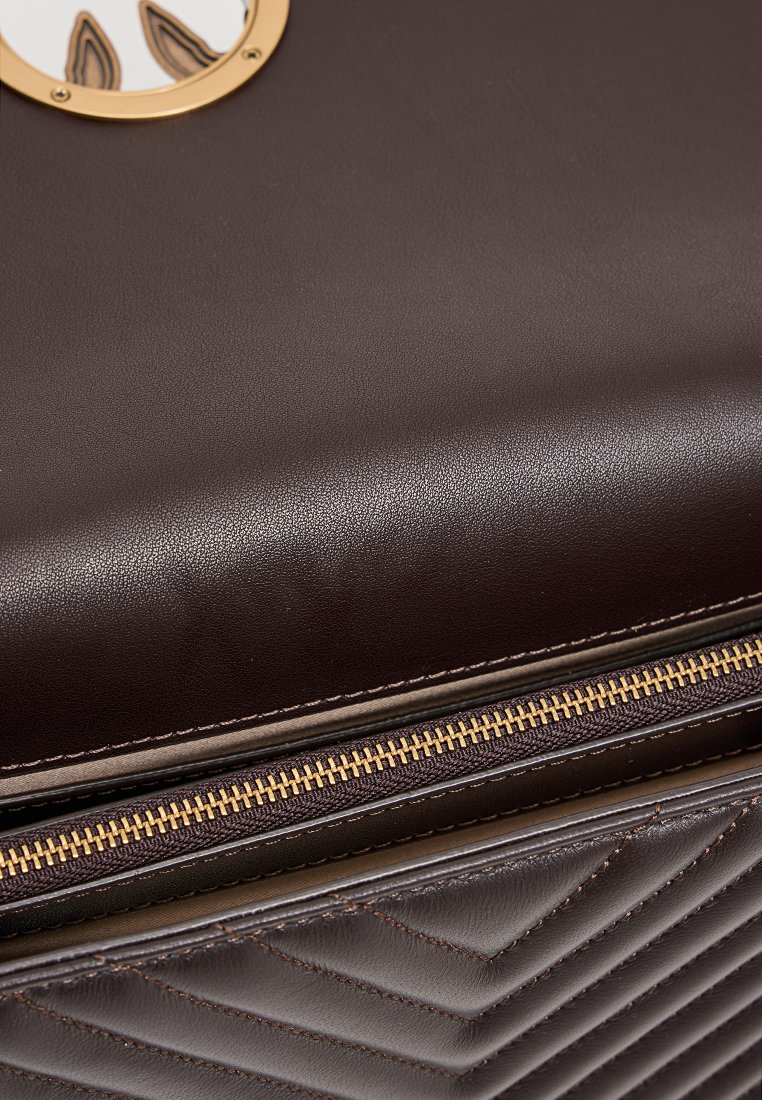 Brązowa skórzana torba o pikowanej fakturze i złotych akcentach. Posiada zamek błyskawiczny i okrągły emblem, co podkreśla jej elegancki design.