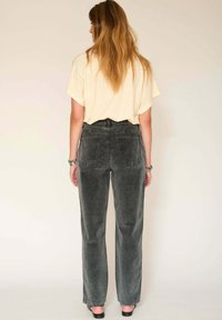 Pantalon en velours côtelé gris avec une coupe droite, doté de deux poches arrière, associé à un haut ample de couleur crème.