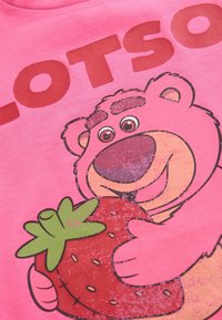 Rosa bomullströja med en tecknad björn som håller en jordgubbe, med stor röd text som säger "LOTSO" ovanför bilden.