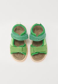 Green children's sandals made of soft fabric and suede, featuring two adjustable Velcro straps, a light brown insole, and a rubber sole.
