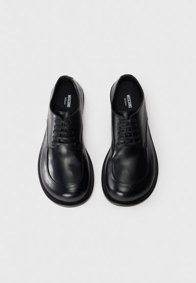 Pantofi negri din piele cu vârful rotunjit, textură netedă, design cu șireturi și cusături contrastante la talpă. Stil minimalist, fără ornamentații.