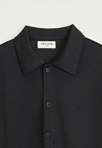 Chemise noire à texture, à manches courtes, avec un col pointu et trois boutons noirs sur le devant, étiquetée taille S par la marque Frilivin.