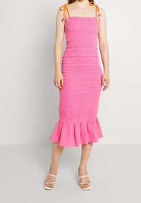 Vestido midi rosa con fruncido y dobladillo con volantes, tirantes spaghetti y lazos naranjas. Presenta un cuerpo ajustado y una tela texturizada.