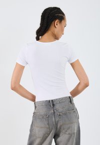 T-shirt blanc ajusté à manches courtes, associé à un jean gris délavé taille haute avec poches arrière et détails de coutures visibles.