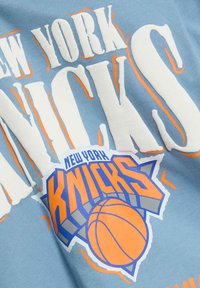 Camiseta de algodón azul claro con texto en blanco y naranja "NEW YORK KNICKS" en negrita, con un logo gráfico de baloncesto y acentos de estrellas.
