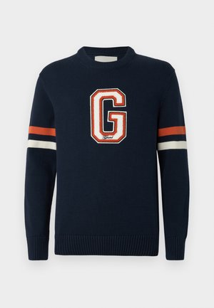 Tumesinine kudumiga sviiter, millel on suur valge ja oranž "G" logo ning oranžide, valgete ja tumesiniste triipudega varrukad. Ribitud varrukasuu.