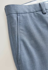 Gros plan sur un pantalon à motif pied-de-poule bleu-gris montrant la ceinture, les passants, la poche latérale et les coutures détaillées.