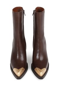 Botas de tornozelo em couro castanho com um formato pontiagudo, apresentando um detalhe em forma de coração dourado na biqueira e um fecho lateral. Textura suave com um acabamento polido.