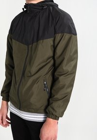 Green and black hooded jacket featuring a zip front, elastic cuffs, and side zip pockets; smooth texture with a color-block design.
