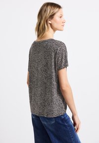 Top a maniche corte in una stampa animale beige e nera. Tessuto fluido con una vestibilità rilassata, scollatura rotonda e orlo posteriore leggermente più lungo.