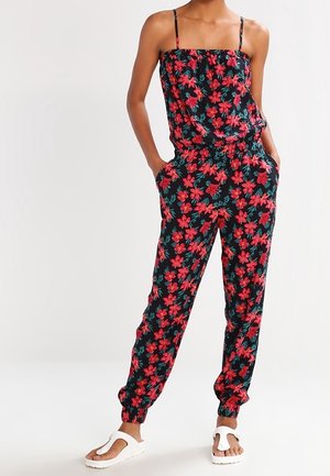 Blomstret jumpsuit med tynde stropper, der har en sort bund med røde blomster og grønne blade. Elastisk taljebånd, tilspidsede ankler, lommer.