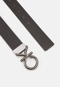 Black leather belt with a textured silver hardware buckle featuring a circular ring and crossed detail; adjustable with multiple holes.