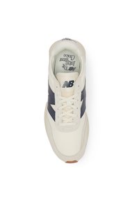 Beige leather sneaker with navy accents, textured side panel, flat laces, and a cushioned insole, featuring a round toe and rubber sole.