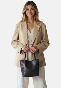 Borsa tote in pelle nera con doppio manico, caratterizzata da una texture liscia e un design minimalista, esposta su uno sfondo chiaro.