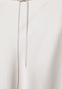 Vêtement blanc avec un cordonnet blanc fin pendant librement sur un fond blanc uni.