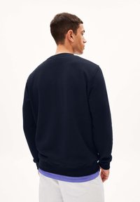 Marineblauwe katoen sweatshirt met een ronde hals, lange mouwen en geribbelde boorden, met een gelaagde paarse shirt aan de zoom en een minimalistisch ontwerp.