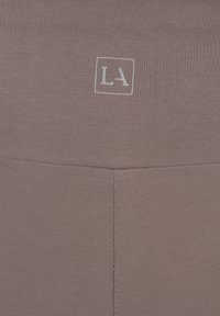 Bruine sportleggings met een geribbelde textuur en een klein wit 'LA' logo binnen een vierkant. Ontworpen met een hoge tailleband.