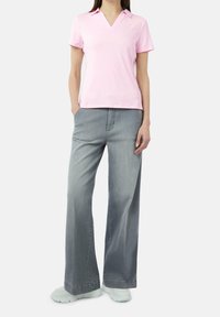 Polo rosa de manga corta con escote en V, combinado con pantalones de mezclilla gris de pierna ancha y zapatillas de color claro, mostrando un estilo casual.