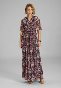 Robe maxi en matériau transparent, présentant un motif géométrique multicolore en rouge, bleu et crème. Col en V, manches courtes et détail de taille à nouer.