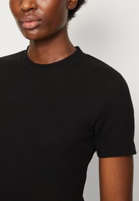 Svart ribbet t-skjorte med rund hals og korte ermer, med en tettsittende design som fremhever teksturen i stoffet.