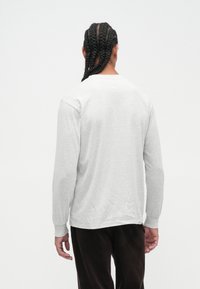 T-shirt grigio a maniche lunghe con una texture morbida, scollatura rotonda e vestibilità leggermente rilassata. Dettagli di cucitura visibili sui polsini e sull'orlo.