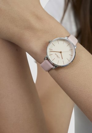 Runde Uhr mit silbernem Gehäuse, pinkfarbenem Lederarmband, cremefarbenem Zifferblatt und roségoldenen Stundenmarkierungen. Minimalistisches Design mit zwei Zeigern.