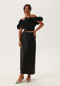 Sort off-shoulder top med flæser på ærmerne og en tætsiddende talje, kombineret med en lang sort nederdel og zebra-stribede hæle.