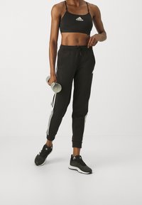Top corto atlético negro y joggers con rayas laterales blancas. Zapatillas negras. Sosteniendo un manillar. Tela suave, diseño ajustado y tirantes ajustables.