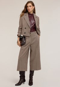 Blazer double boutonné à carreaux marron sur un top en simili cuir bourgogne, associé à un pantalon large et des bottes à talons marron hauteur genou.