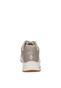 Zapatilla deportiva beige con una parte superior de cuero suave, entresuela blanca y suela de goma de color marrón. Cuenta con un cuello acolchado y acentos de diseño minimalista.
