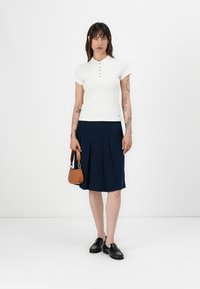 Bílá polokošile se zlatými knoflíky, doplněná námořnickou plisovanou sukní. Černé boty a hnědá kabelka dotvářejí celý outfit.
