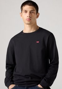 Černé tričko s dlouhým rukávem a kulatým výstřihem; na hrudi malý červený logo Levi's. Vyrobeno z bavlny; hladká textura a pohodlný střih.