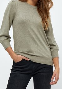 Ljus olivgrön stickad tröja med rund halsringning, trekvartslånga ärmar, ribbade muddar och avslappnad passform. Bärs med svarta jeans.