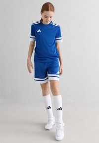 Blå sportsdrakt og shortser med hvite striper, med tre striper på ermene og logo. Hvite sokker og fotballsko fullfører antrekket.