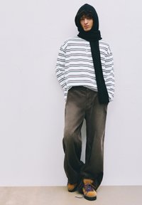 Gestreiftes Langarmshirt in Weiß, Marineblau und Rot, kombiniert mit weit geschnittenen braunen Cordhosen. Schwarzer Schal und braune Schuhe mit blauen Schnürsenkeln.