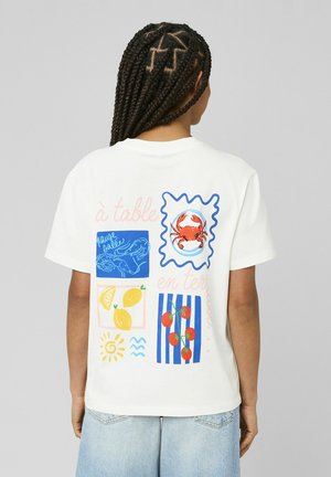 Personne aux cheveux tressés portant une chemise blanche avec des illustrations colorées d'aliments comprenant un crabe, un citron, des crevettes et des tomates cerises dans le dos.