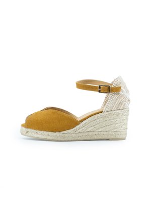 Sandale à talon compensé en espadrille avec un dessus en velours côtelé moutarde et un dos tissé texturé. Elle est dotée d'une bride de cheville avec une boucle en métal et d'un talon en jute.