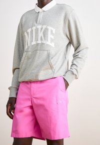 Gray sweatshirt with a white Nike logo, featuring a collar and front pocket. Paired with bright pink shorts, also with a small Nike logo.