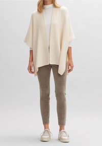 Krémový žebrovaný cardigan s otevřeným předním dílem, batwing rukávy, střední délka, v kombinaci se světle béžovými slim kalhotami a bílými teniskami.
