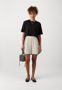 Tricou negru scurt, pantaloni scurți crem cu margini ondulate, balerini negri, ținând o mică geantă de mână cu model. Ținută simplă și casual.
