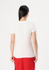 Weißes T-Shirt mit kurzen Ärmeln aus weicher Baumwolle, mit einem Rundhalsausschnitt und schmaler Passform, getragen mit einem roten Rock.