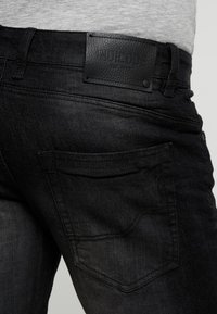 Jeans in denim nero con un'etichetta in pelle con il marchio "INDICODE", tasche posteriori standard e un design slim fit. Tessuto testurizzato.