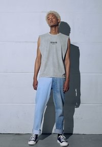 Szary bezrękawnik z napisem "moon", połączony z jasnoniebieskimi tapered jeansami. Białe trampki z czarnymi akcentami. Gładkie faktury i luźny krój.