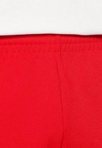 Röda atletiska shorts gjorda av stretchigt tyg; med resårmidja och slät textur utan synliga mönster eller accenter.