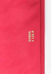Tela textil roja con una textura suave, con "BIMBA Y LOLA" grabado en dorado en la esquina inferior derecha.