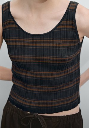 Zbliżenie na osobę ubraną w bezrękawnik w czarno-brązowe paski, połączony z ciemnobrązowymi spodniami dresowymi z troczkami.