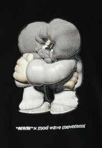 Un gráfico sobre una tela negra presenta un personaje estilizado con ropa texturizada gris, zapatos blancos y un texto bordado debajo.