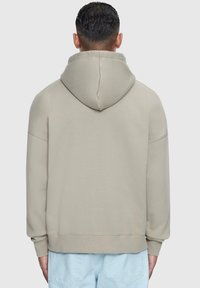 Beige hettegenser med løs passform, ribbede mansjetter og kant. Mykt stoff med glatt tekstur, synlige sømmer langs skuldersømmene.